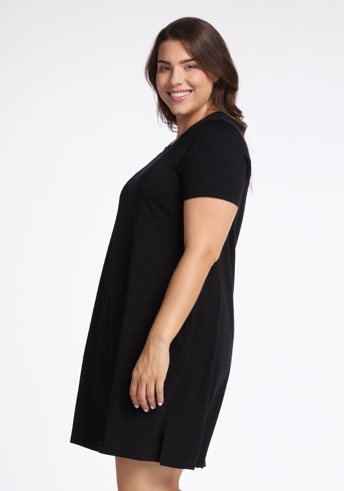 A person with long dark hair smiles in profile, wearing a short-sleeved Woolx Georgie Dress - Black against a white background.