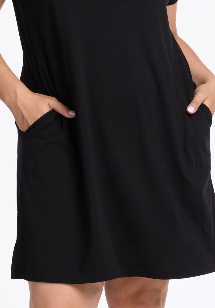 Close-up of a person in a Woolx Georgie Dress - Black, featuring hands in the side pockets. The knee-length A-line dress, made from soft merino wool, pairs beautifully with their light gray nails.