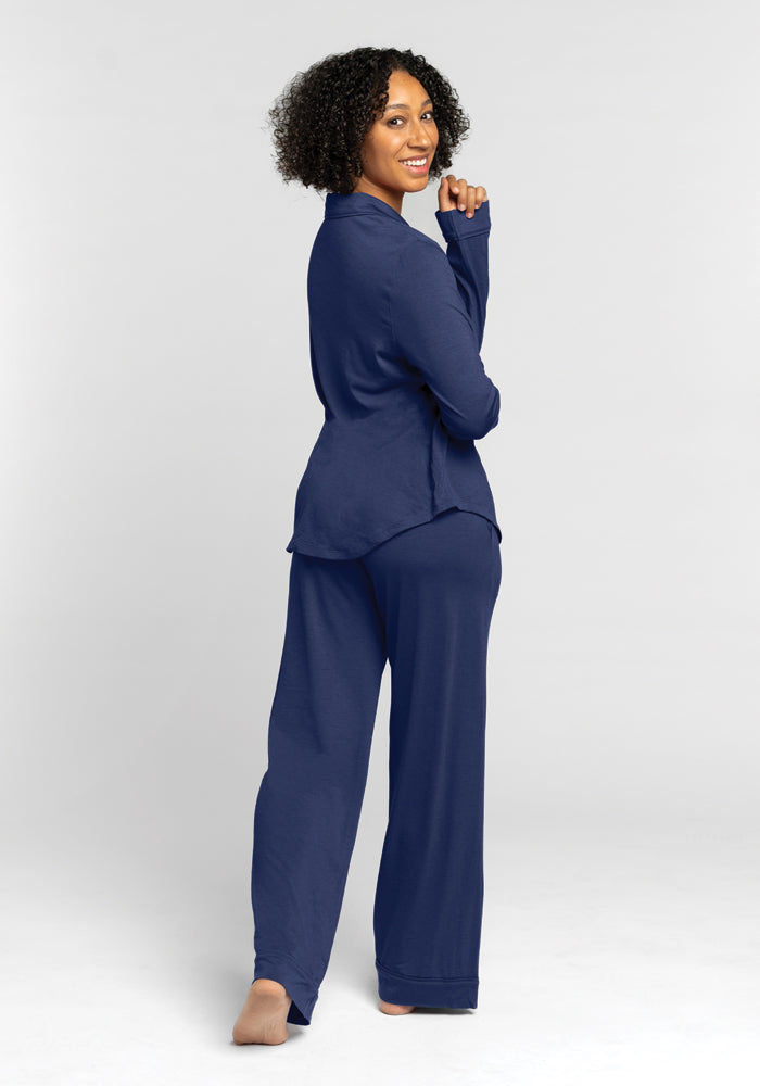 A person with curly hair smiles while looking back over their shoulder, wearing the relaxed-fit Harper FeatherTouch® Pajama Set in Starry Night by Woolx. They stand barefoot against a plain white background.