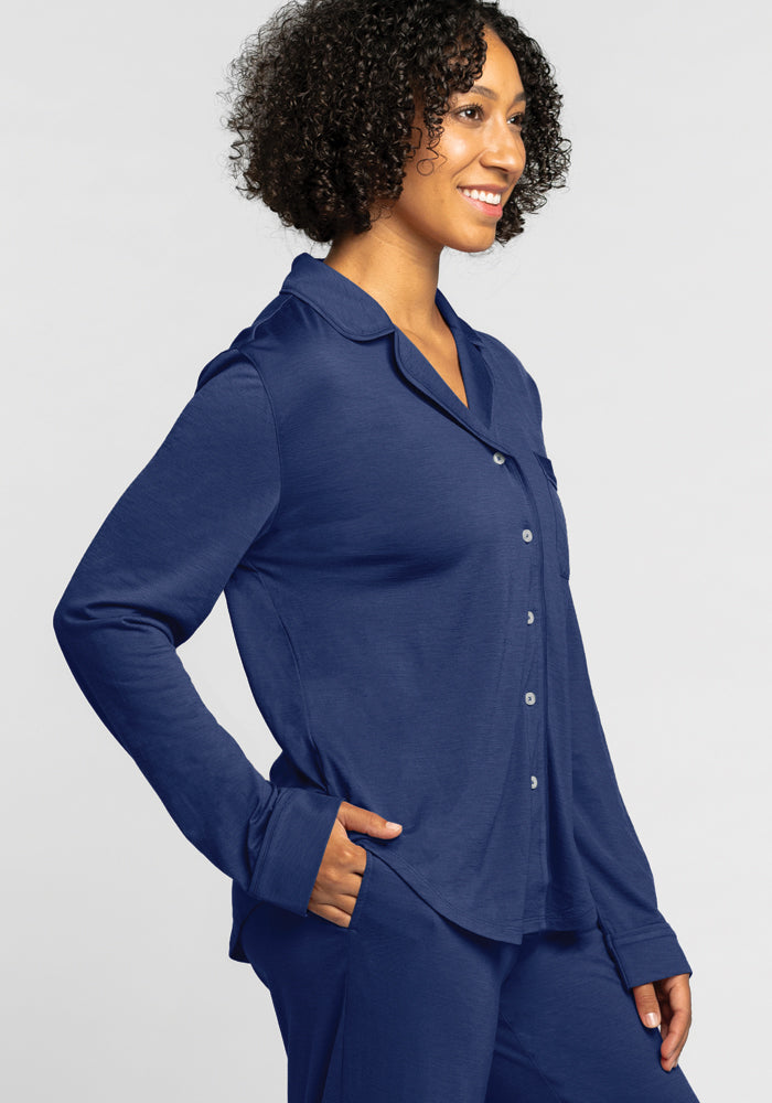 A person with curly hair is smiling and standing sideways, dressed in the Harper FeatherTouch® Pajama Set - Starry Night by Woolx in a relaxed fit. The background is plain gray.