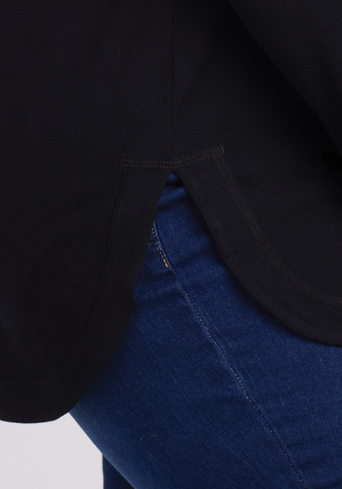 Close-up of someone in blue jeans and Woolx's Hazel Tunic - Black, featuring a curved hem. This sleek, temperature-regulating Merino wool top highlights rich fabric textures for unmatched comfort and style.