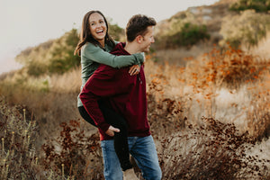 Couple wearing woolx in a field and man is carrying the woman on his back