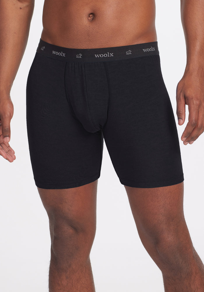 A person is seen wearing black Jazzy No Fly Boxer Briefs from Woolx, standing against a plain white background. The waistband prominently features the "Woolx" label, emphasizing the fit and style of these boxer briefs.