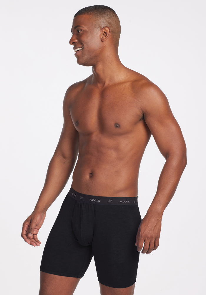 A man stands against a white background, smiling and looking to the side in black Jazzy No Fly Boxer Briefs. The waistband proudly showcases the brand name "Woolx," highlighting the stylish, lightweight wool design.