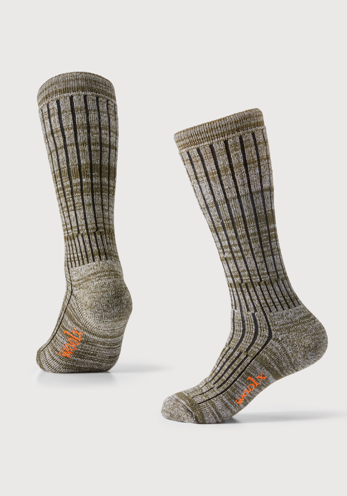 A pair of Woolx's Joey Socks in Dark Forest Marled, featuring a ribbed pattern and a contrasting orange logo near the toes. One sock stands upright while the other is laid on its side, showcasing the luxurious blend of fabrics against a white background.