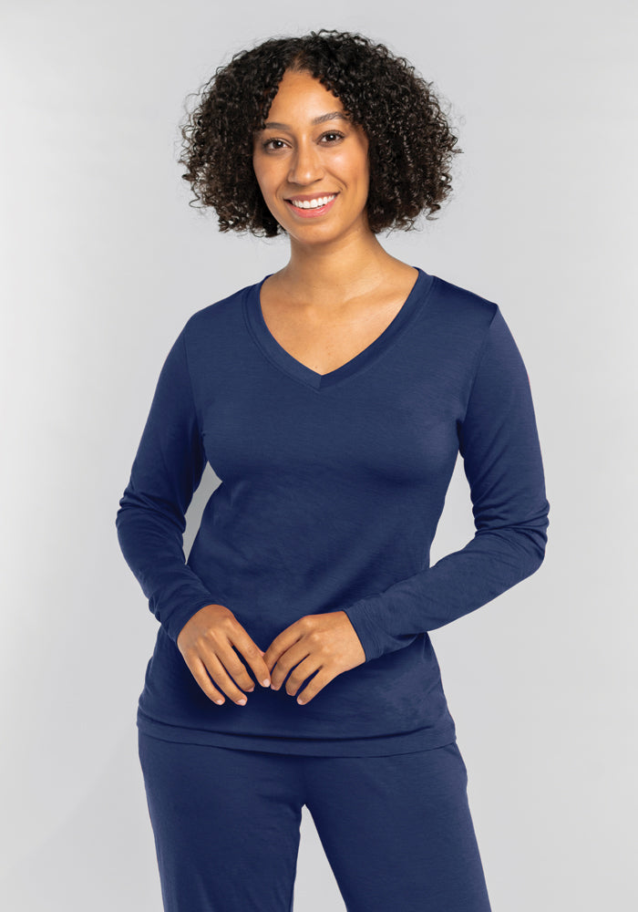 A person with curly hair smiles while wearing a navy blue Lily V Neck Lounge Top - Starry Night and matching pants by Woolx, standing against a light gray background. 