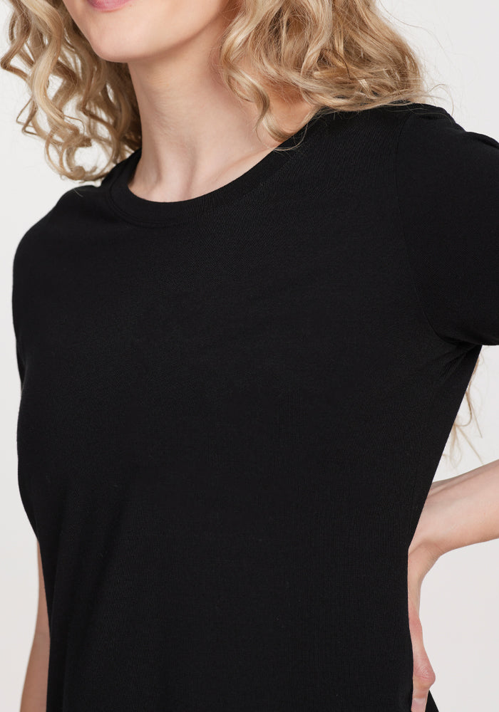 A person with curly blonde hair wears a black tee resembling the Woolx Lexie Dress & Cover-up. They confidently stand with one hand on their hip against a crisp white background, shown cropped from shoulders down.