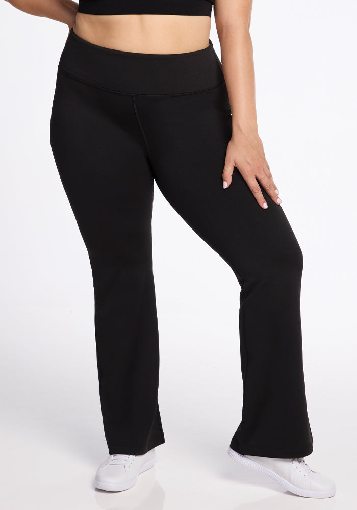 A person is wearing the Marissa Pants in black from Woolx and white sneakers, standing with one hand resting on their thigh against a plain white background.