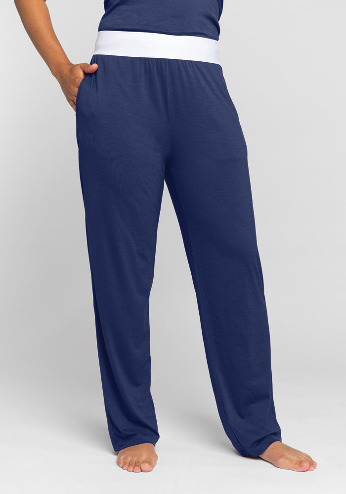 The individual is wearing the Woolx Maya Lounge Pants in the Starry Night color, which features a loose fit and a comfortable white waistband. They are standing barefoot against a plain light background, with their left hand tucked into one of the pants' pockets. 