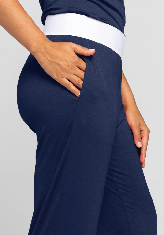 The image features an individual wearing the Woolx Maya Lounge Pants in Starry Night, highlighting the side profile. The person’s hand is casually placed in the pocket of these moisture-wicking pants against a neutral background.