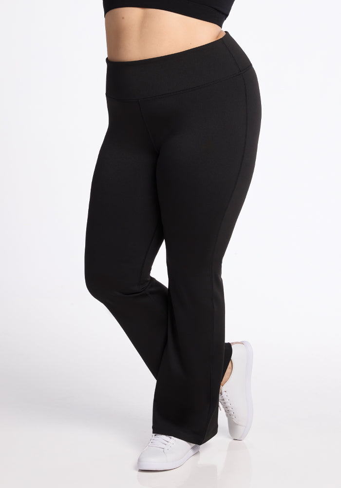 A person wearing the Marissa Pants in Black by Woolx and white shoes stands against a plain background. The pants flare slightly at the bottom, and their top is cropped out of the image.