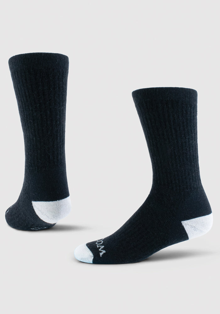 Displayed against a plain light background are two Core Crew Socks Full Cushion - Black by Woolx. Made from Merino wool, these socks feature white toes and heels and are shown at different angles to emphasize their ribbed texture and performance fit.