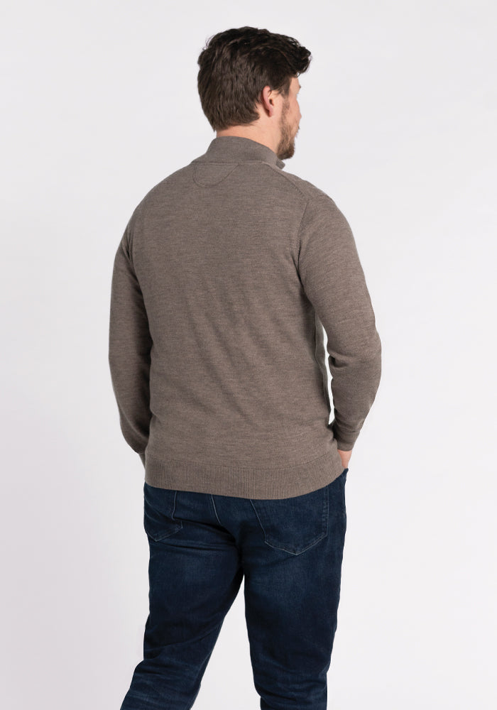 A man with short brown hair is standing and facing away. He is wearing the Woolx Enzo Quarter Zip sweater in Sable and dark blue jeans.