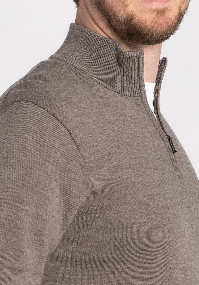 A close-up of a person wearing the Enzo Quarter Zip - Sable sweater from Woolx, showcasing its taupe color and ribbed collar with a subtle horizontal texture. The person's face is not visible in the image.