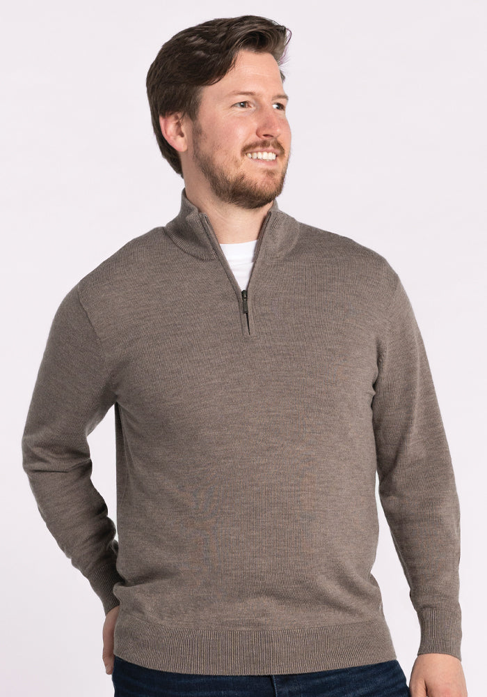 A smiling man with short hair and a beard is looking to the side. He is wearing the Enzo Quarter Zip in Sable from Woolx over a white shirt, against a plain white background.