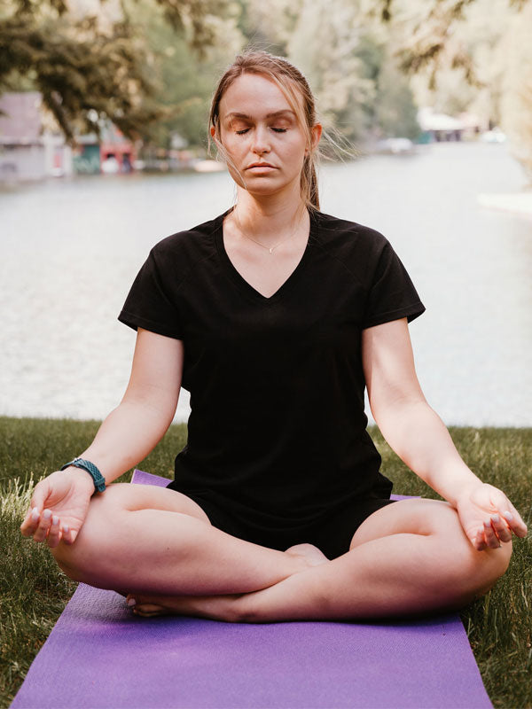 Model wearing black Mia tee while meditating on yoga mat