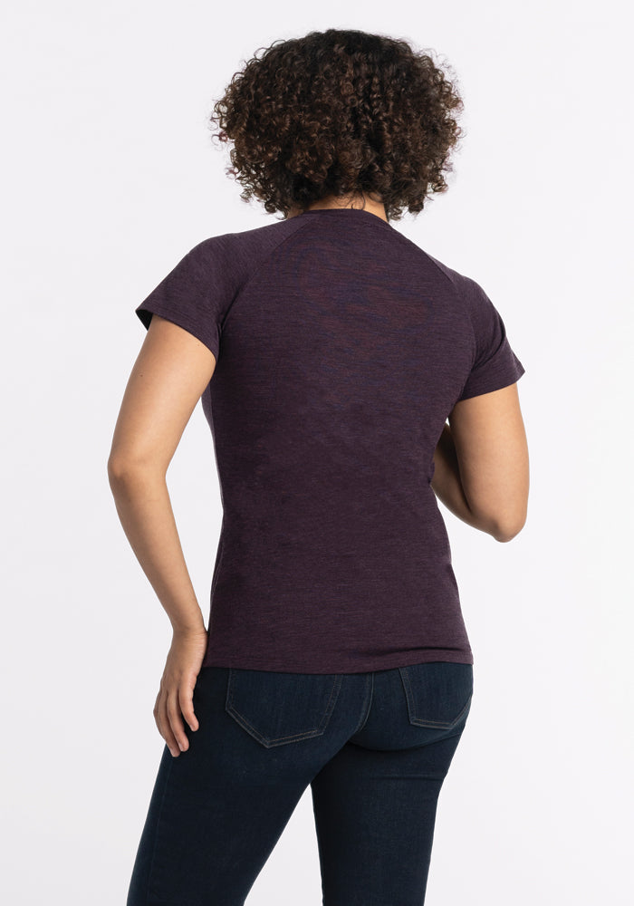 Rear view of a person with curly hair wearing a Woolx Mia V Neck in deep plum and dark jeans, standing against a plain white background.