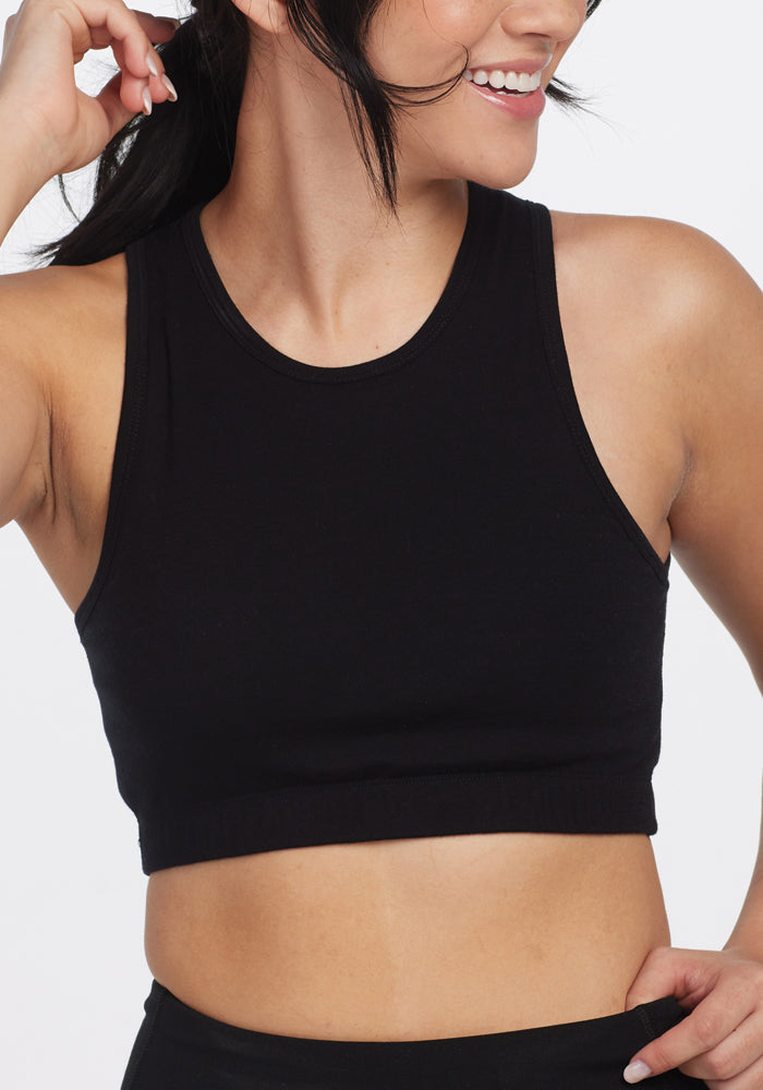 A person wearing a Woolx Mila Bra - Black, smiles while looking to the side. Their hair is tied back as they pose against a plain white background.