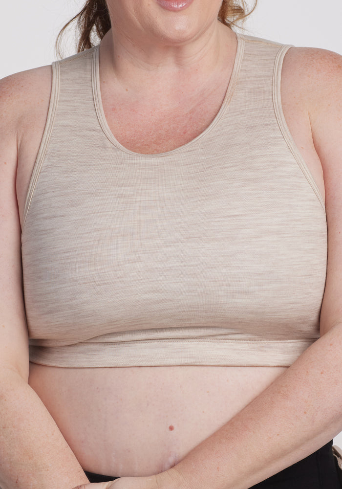 A person in a light beige tank top, echoing the Woolx Mila Bra in Cream Heather, stands confidently with arms crossed against a plain white background, shown from shoulders to waist.