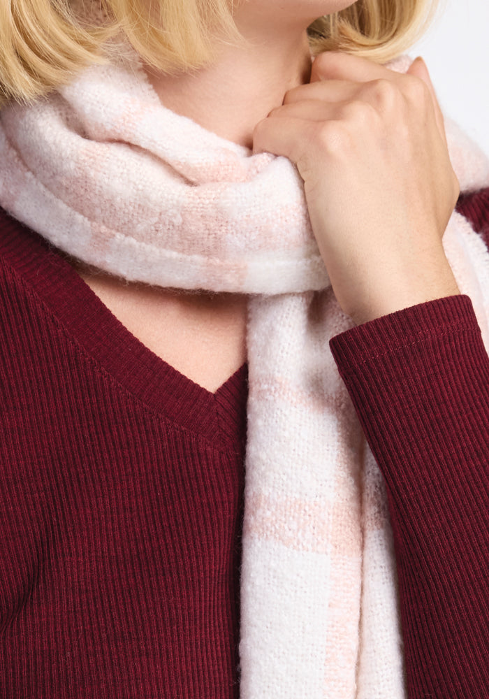 A person wearing a Bradie Scarf in Mauve Plaid from Woolx over a burgundy ribbed sweater is holding the scarf near their neck with one hand. The focus is on the texture and color of the clothing.