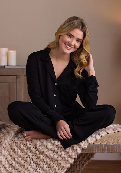 A person adorned in a beige crop top and the Mary Kate Lounge Pants in Chocolate Plum by Woolx, crafted from FeatherTouch fabric, stands barefoot. The pants come with an elastic waistband, drawstring, and pockets, making them perfect for travel lounge wear. The minimalist white background highlights the comfort-focused look.