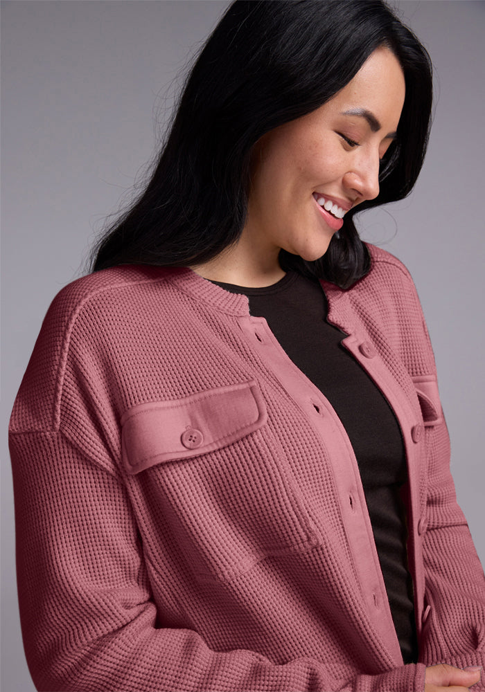 A person with long dark hair smiles while looking downward. They are wearing the Oaklynn Waffle Shacket in Wild Ginger by Woolx over a black top, set against a plain gray background.