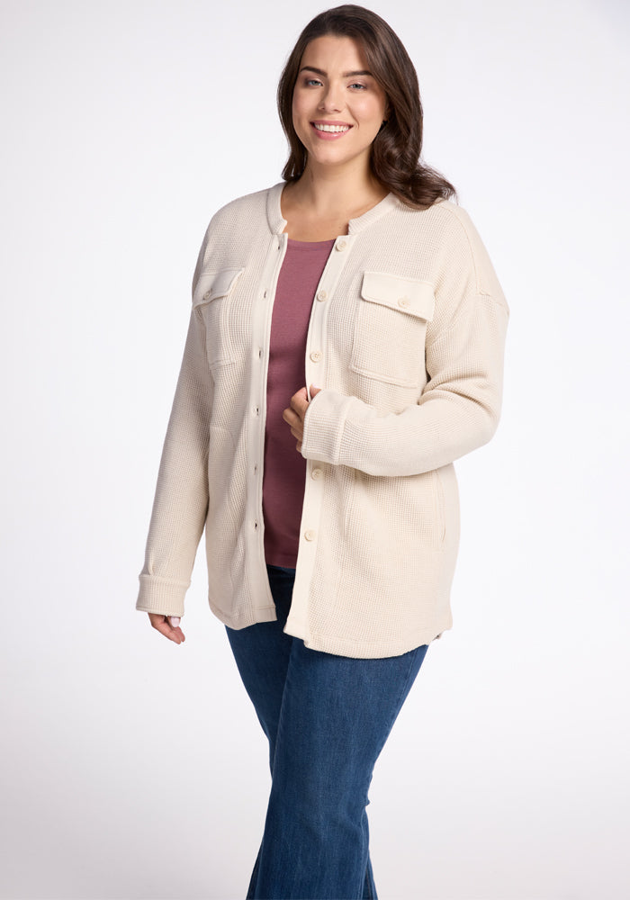 A person wearing the Oaklynn Waffle Shacket in oatmeal by Woolx over a mauve shirt and blue jeans, smiling against a plain white background. 