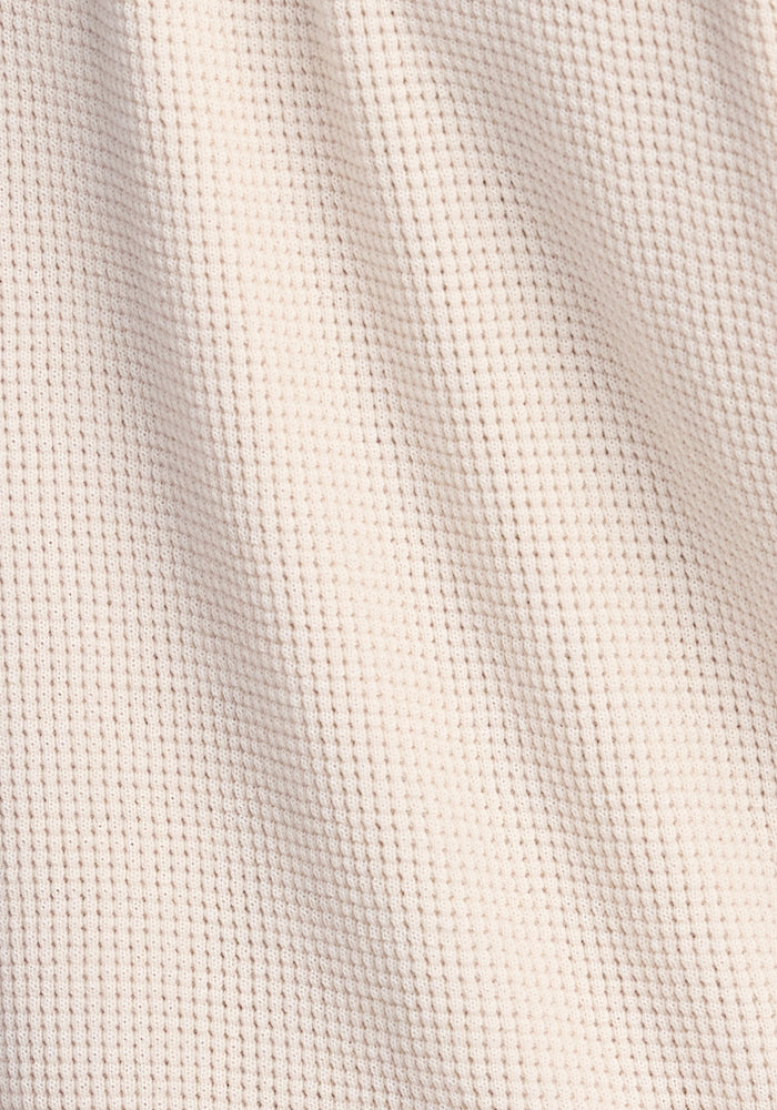 Close-up of the Oaklynn Waffle Shacket in oatmeal by Woolx, showcasing its textured, off-white waffle knit fabric with a grid-like pattern. The material appears soft and slightly wrinkled, highlighting its comfort and versatility for any season.