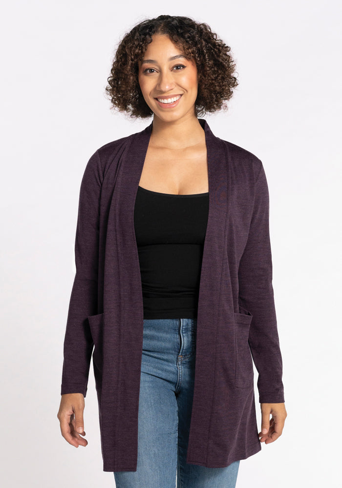 A person with curly hair smiles while wearing the Woolx Paisley Cardigan in Deep Plum, crafted from Australian Merino Wool, over a black top and blue jeans. They stand against a plain white background. 