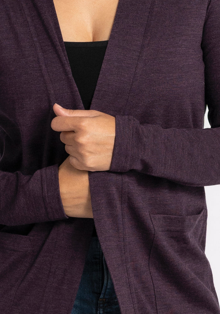 Close-up of a person wearing a Woolx Paisley Cardigan in Deep Plum over a black top, holding the edge of the cardigan. Made from premium Australian Merino Wool, they are standing against a neutral background. Only the torso and hands are visible.