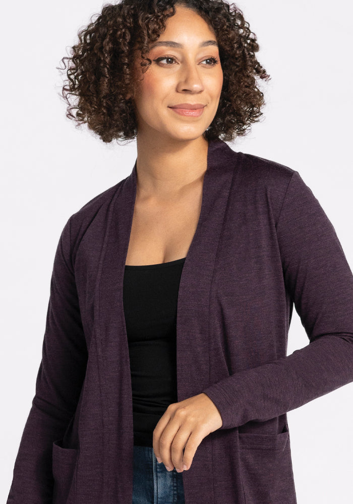 A person wearing the Woolx Paisley Cardigan in Deep Plum and a black top is smiling softly while looking to the side. They have curly hair and are standing against a plain, light background.