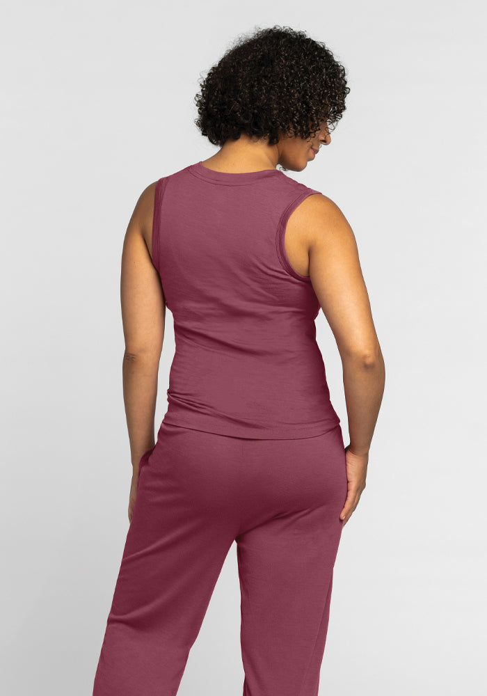 A person with curly hair stands with their back to the camera, wearing the Phoebe Lounge Tank in Wild Ginger from Woolx, along with matching pants. Crafted from cooling comfort fabric, this outfit beautifully complements the plain background.