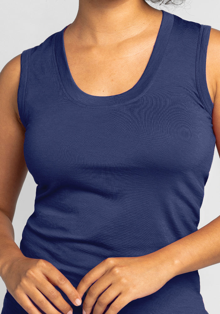 A person wearing the Phoebe Lounge Tank - Starry Night by Woolx, a navy blue top made from merino wool, stands against a plain background. With their hands lightly clasped in front, the temperature-regulating fabric of this sleeveless tank ensures comfort, highlighting only their upper body.