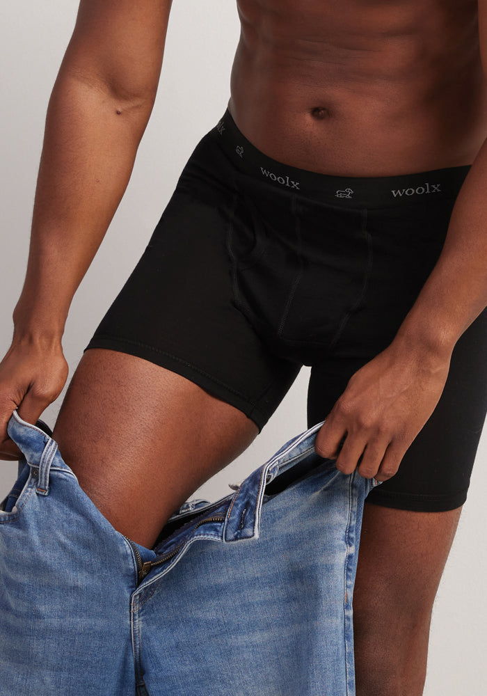 A person wearing Woolx Reaction Boxer Briefs - Black is pulling up a pair of blue jeans. The image focuses on the lower body, emphasizing the ultra-durable fabric of the underwear along with the jeans.