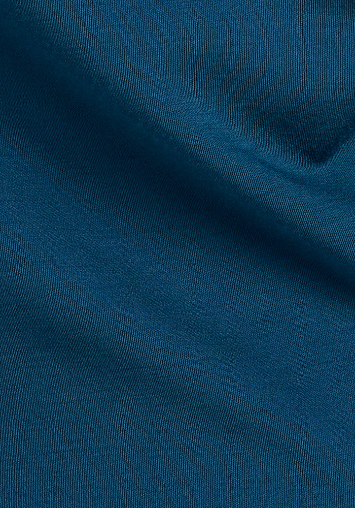 A close-up of the blue textured fabric, presumably the luxurious Merino Wool from Woolx's Elena V Neck - Real Teal collection, highlights its smooth weave and subtle sheen. The light creates soft shadows and highlights, emphasizing the material's softness and quality in a Relaxed Fit style.