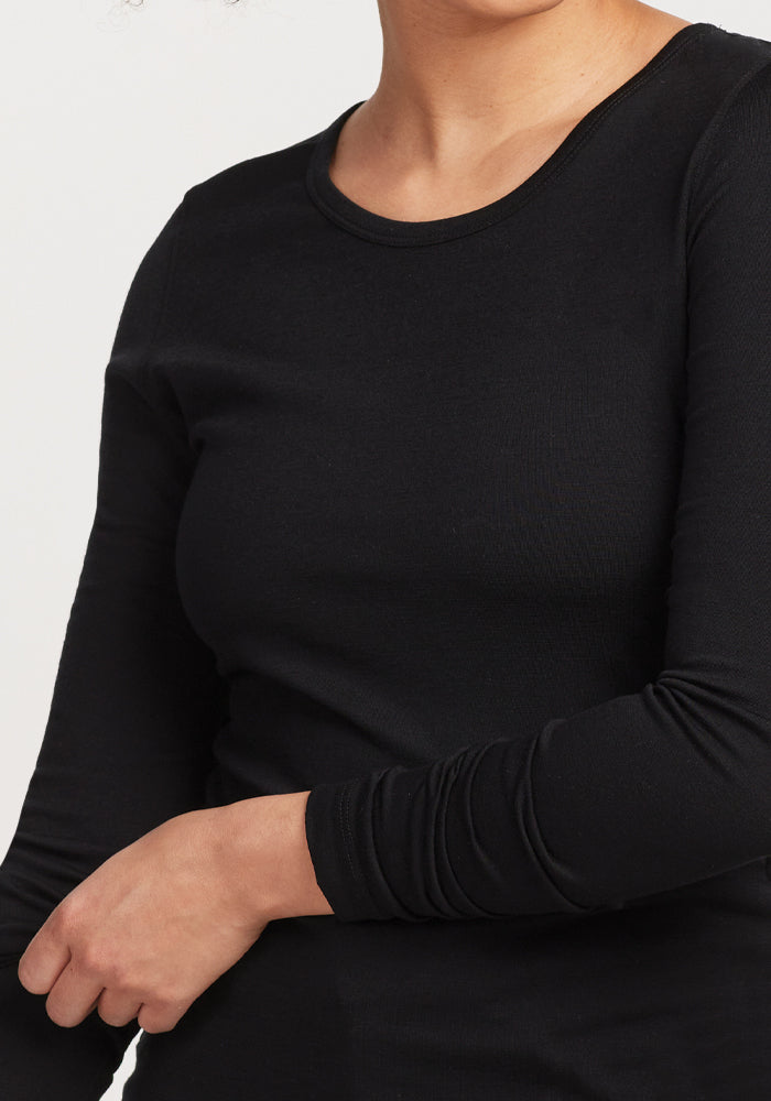 A person wearing the Remi Long Sleeve T-Shirt in black by Woolx, crafted from moisture-wicking Merino wool, stands against a plain background.