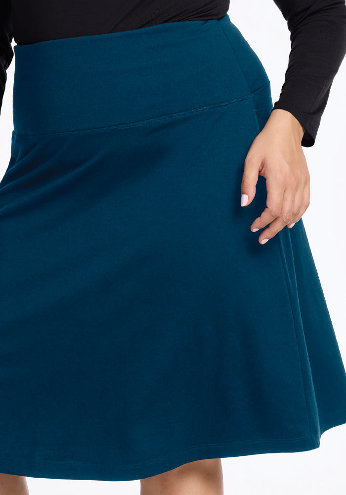 A person is pictured wearing the Woolx Marilyn Flowy Midi Skirt in Real Teal, paired with a black long-sleeved top. Their hand rests gracefully on the side of the skirt, accentuating its exquisite detailing and A-line design.