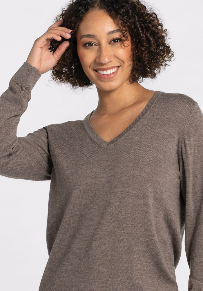 Smiling person with curly hair wearing the Francesca Sweater in Sable from Woolx against a light background.