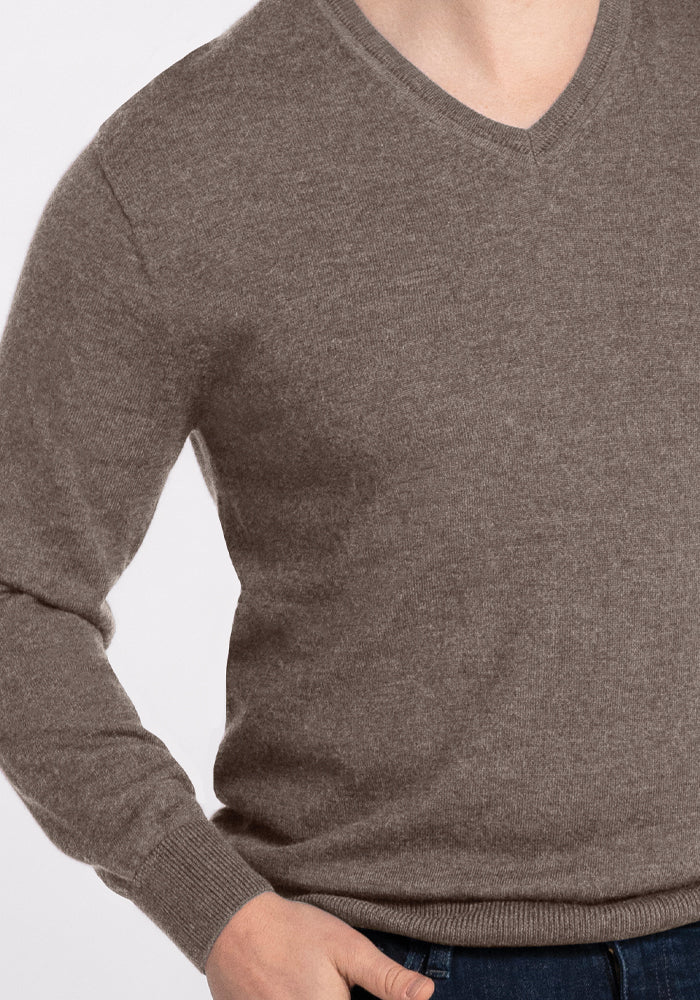 A person wearing the Woolx Vincenzo Sweater in Sable paired with jeans, with their left hand placed in the pocket, against a light gray background.