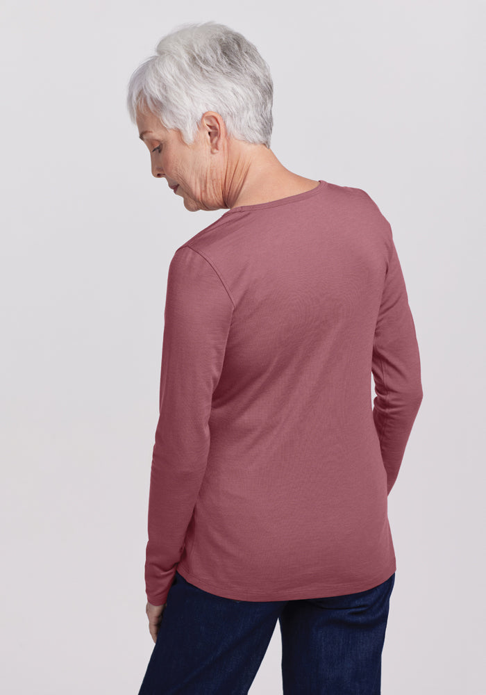 An older adult with short gray hair is wearing a Woolx Remi Long Sleeve T-Shirt in Wild Ginger, paired with dark pants. They're facing away from the camera against a plain light background, exuding an air of comfort and ease.