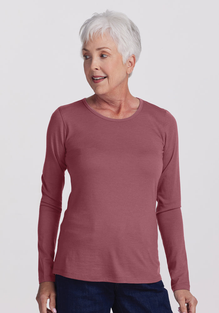 A person with short white hair is wearing the Remi Long Sleeve T-Shirt in Wild Ginger from Woolx, paired with dark blue jeans. They are standing against a plain light background, looking to the side with a slight smile.