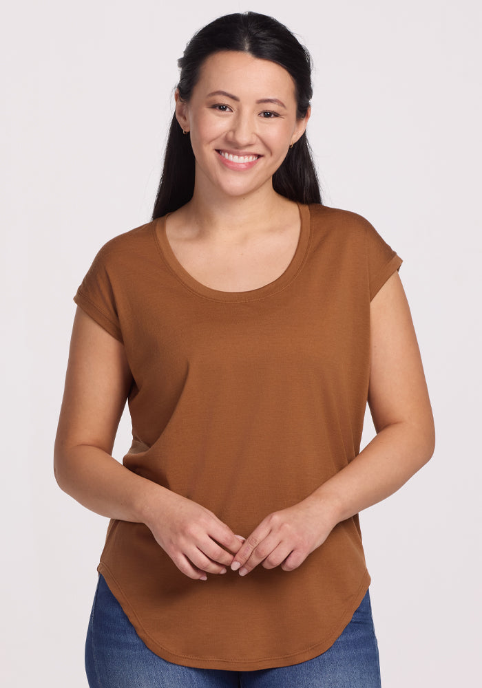 A person with long dark hair is wearing the Woolx Gabi Tunic Top in Sahara Dust and blue jeans, smiling against a plain white background. 