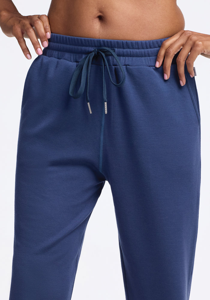 A person wearing Woolx's Parker Sweatpants in the Starry Night color stands with hands on the waistband. These temperature-regulating jogger pants, which feature a drawstring, reveal a visible midriff against a plain white background, highlighting their functionality and stylish odor-free design.