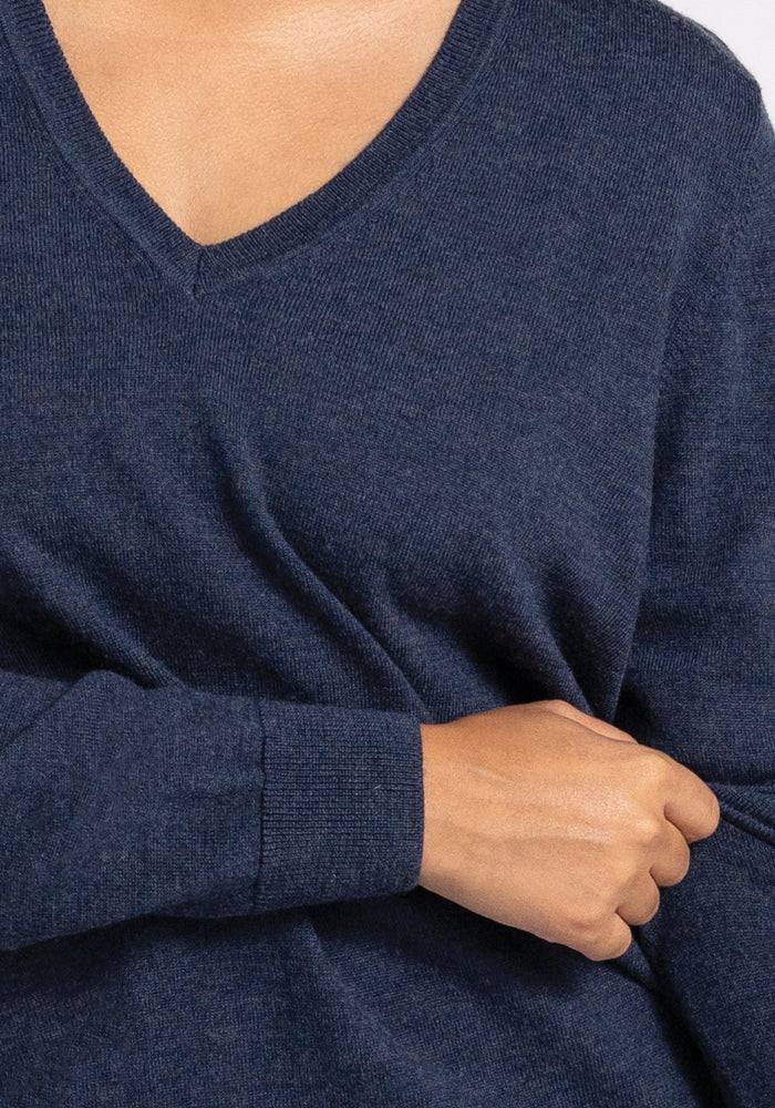 A person wearing the Francesca Sweater in Twilight Storm from Woolx holds the fabric slightly with one hand, highlighting the luxurious texture and fit of this Merino wool garment.