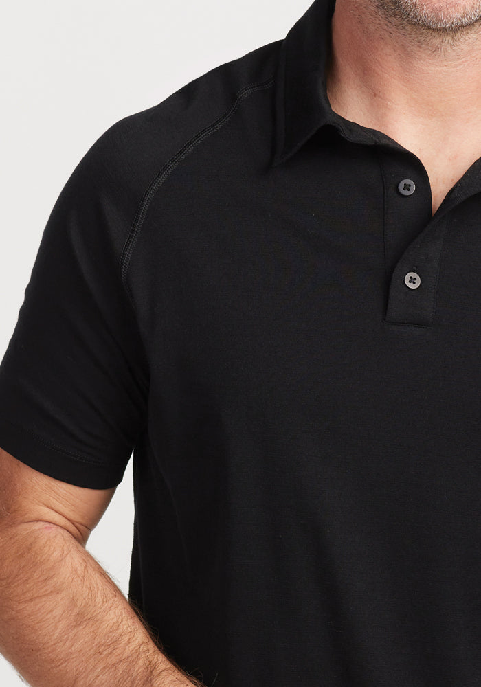 A person in a Summit Polo - Black by Woolx, crafted with moisture management and high-performance athletic gear features, stands confidently with one arm slightly bent at the elbow. The image focuses on the upper body and shirt details, cropped at the shoulder and chin.