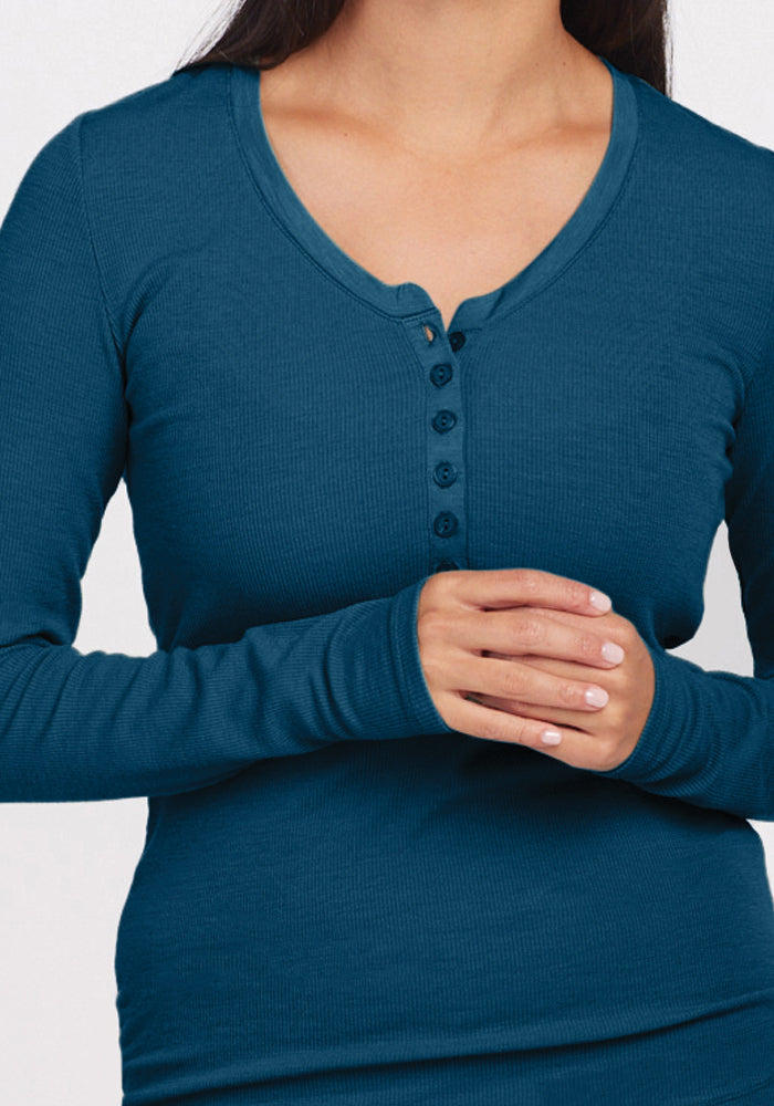 A person wearing the Reese Ribbed Henley in Real Teal from Woolx, designed with moisture-wicking Merino wool. The button-front V-neck enhances their gently clasped hands against a plain, neutral backdrop that underscores the fabric's elegance.