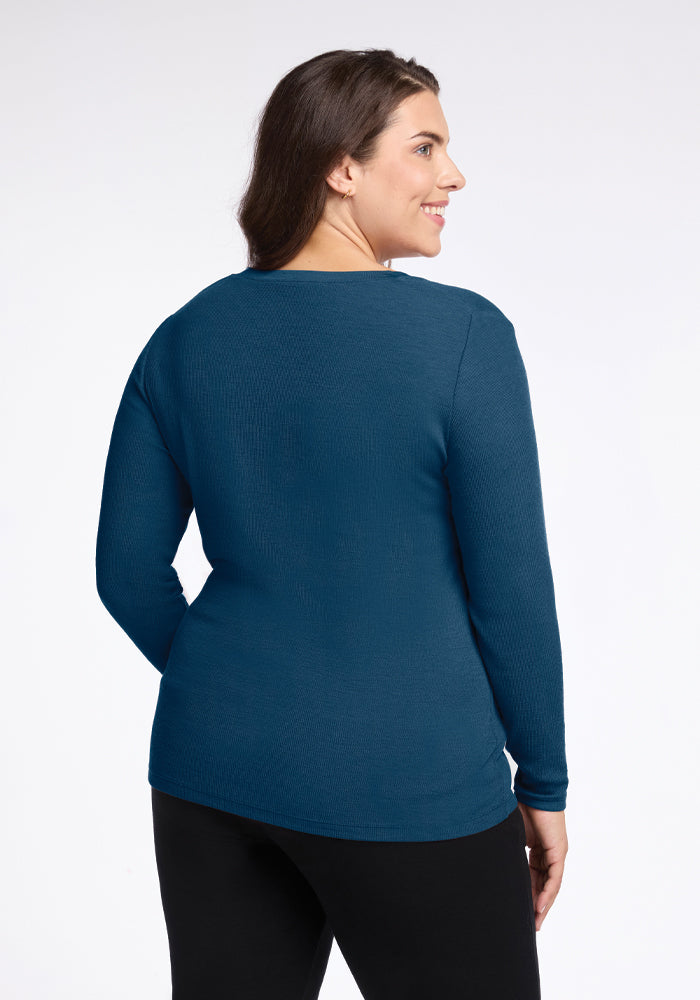 A person stands sideways, facing away from the camera, wearing a Woolx Reese Ribbed Henley in Real Teal and black pants. The ribbed texture adds depth to the simple design against the plain white background.