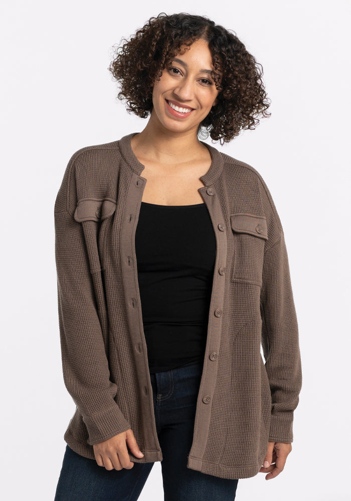 A person with curly hair smiles while wearing the Oaklynn Waffle Shacket in Latte from Woolx over a black top and jeans. The background is plain white. 