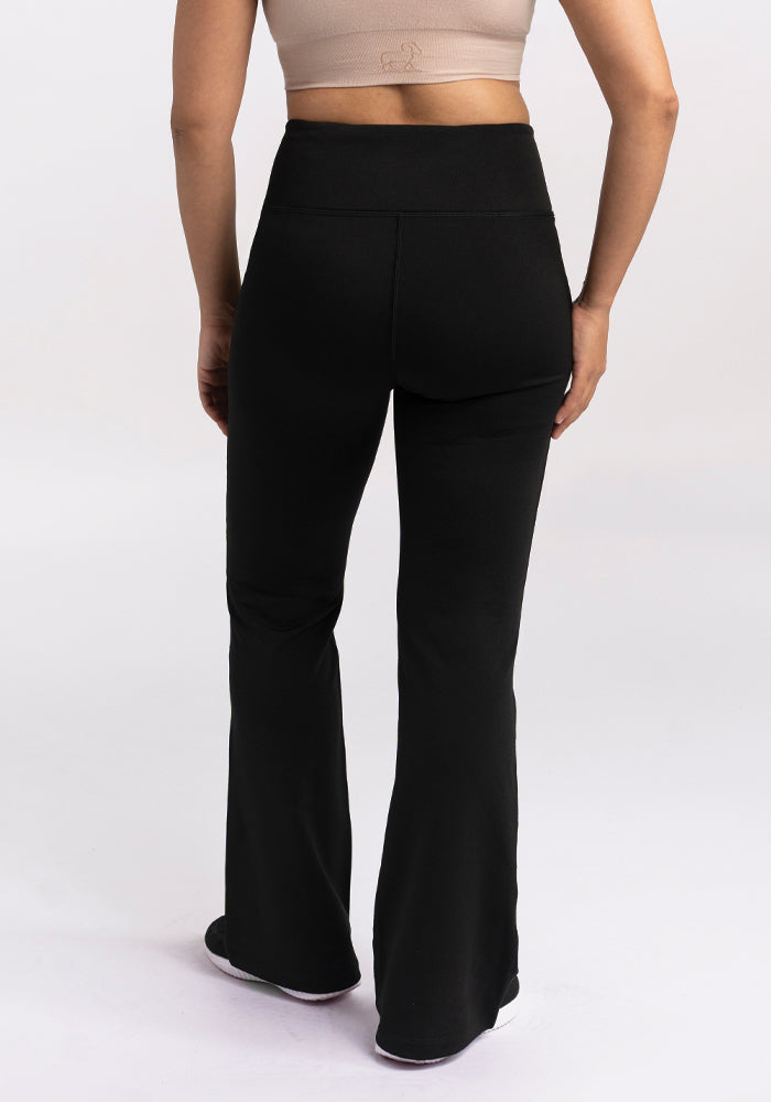 Someone is styled in the Marissa Pants - Black by Woolx, featuring a high-waisted, flared bootcut design paired with a beige crop top. The MerinoFlex® fabric offers an odor-resistant finish, and the picture is captured from behind against a simple background.