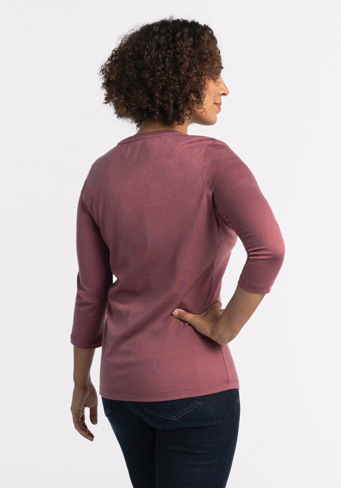 A person with curly hair stands facing away, wearing the Woolx Jenny 3/4 Sleeve Crew Neck in Wild Ginger and dark jeans against a plain white background.